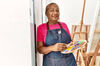 Kıdemli Afro-Amerikan kadın sanat stüdyosunda kendine güvenerek gülümsüyor.