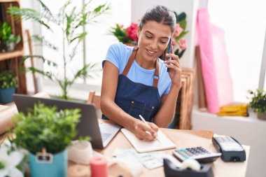 Çiçekçide, çiçekçide, güzel İspanyol bir çiçekçi akıllı telefondan not defterine yazı yazıyor.