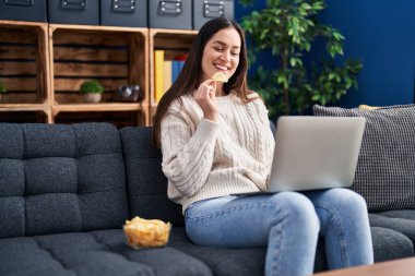 Akıllı telefon kullanan ve evde cips yiyen genç bir kadın.