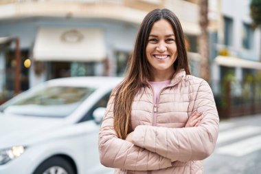 Kendine güvenen genç bir kadın caddede kollarını kavuşturmuş duruyor.