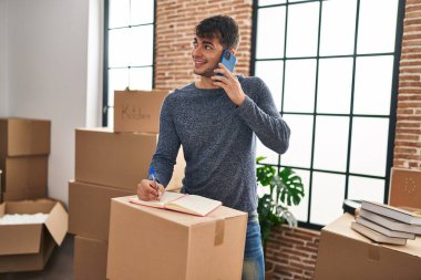 Genç İspanyol adam akıllı telefondan konuşuyor. Yeni evindeki defterde yazıyor.