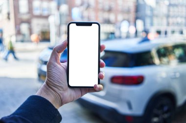 Akıllı telefon tutan adam araba parkında beyaz boş ekran gösteriyor.