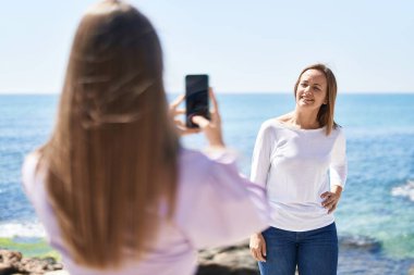 İki kadın anne ve kız deniz kenarında akıllı telefonla fotoğraf çekiyor.