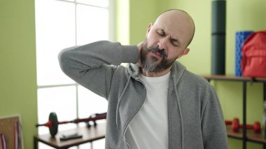 Spor merkezinde boyun ağrısı çeken kel genç bir adam.