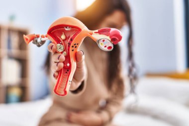 Genç İspanyol kadın yatakta oturuyor. Yatak odasında adet sancısı çekiyor.