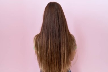 Güzel esmer kadın pembe arka planda dikiliyor. Arkaya bakıyor ve kollarını kavuşturuyor. 