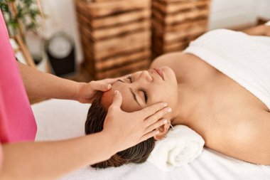 Young beautiful hispanic woman lying on table having head massage at beauty salon