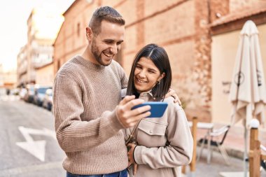 Man and woman couple smiling confident using smartphone at street