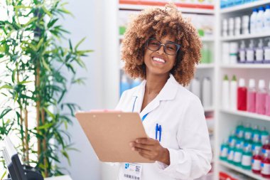 African american woman pharmacist smiling confident writing on document at pharmacy