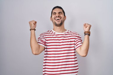 Tecrit edilmiş arka planda duran uzun saçlı İspanyol adam kolları havada ve gözleri kapalı bir şekilde başarıyı kutluyor ve hayrete düşüyor. Kazanan konsept. 