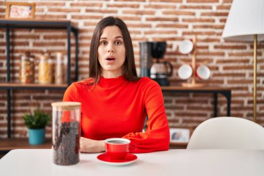 Genç İspanyol kadın evde kahve içiyor. Korkmuş ve ağzı açık, şaşırmış ve şaşırmış. 