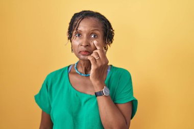 Sarı arka planda duran Afrikalı kadın jestini izlerken gözüne işaret ediyor. Şüpheli bir ifade. 