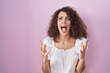 Pembe arka planda kıvırcık saçlı İspanyol kadın deli gibi bağırıyor ve agresif bir ifade ve kollarla bağırıyor. hüsran kavramı. 