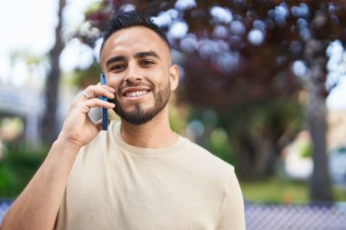 Genç İspanyol adam gülümsüyor. Parktaki akıllı telefondan konuşuyor.