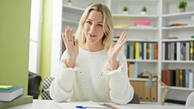 Kütüphane üniversitesinde masada oturan genç sarışın kız öğrenci.