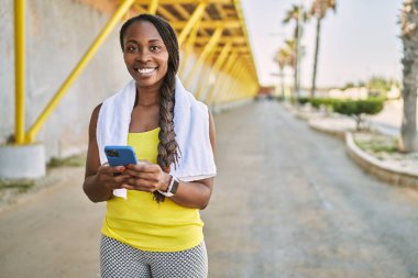 Afro-Amerikalı kadın spor giyer, sokakta akıllı telefon kullanır.