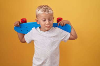 Küçük beyaz çocuk kaykay tutuyor ağzıyla balık suratı yapıyor ve şaşı bakıyor, çılgın ve komik.. 