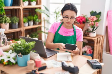 Young hispanic woman florist using laptop and calculator at florist