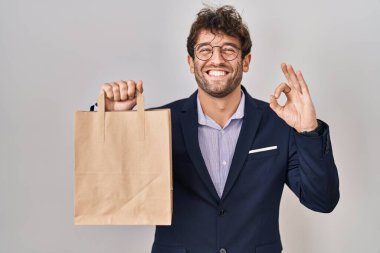 İspanyol iş adamı teslimat çantası tutuyor. Parmaklarıyla imza atıyor, gülümsüyor. Mükemmel bir sembol. 