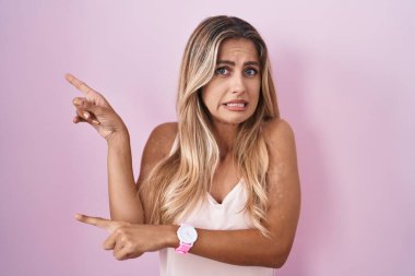 Pembe arka planda duran genç sarışın kadın endişeli ve gergin olduğunu gösteriyor. Endişeli ve şaşırmış bir ifadeyle. 