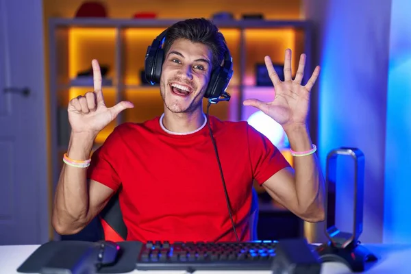 Молодой Латиноамериканец Играет Видеоигры Показывая Показывая Пальцами Номер Семь Улыбаясь — стоковое фото