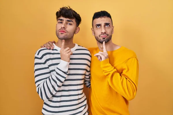 Sarı Arka Planda Dikilen Genç Spanyol Eşcinsel Çift Parmakları Çenesinde — Stok fotoğraf