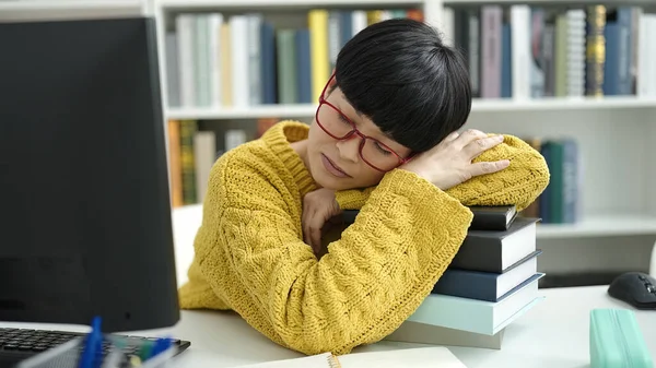 Young chinese woman student leaning on books sleeping at library university