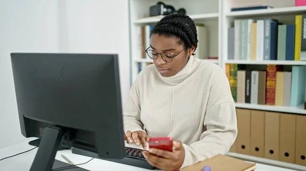 図書館大学でコンピュータとスマートフォンを使うアフリカ系アメリカ人女性学生 — ストック写真