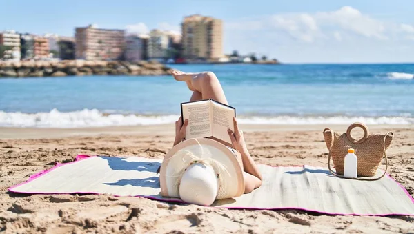 若いですヒスパニック女性身に着けていますビキニと夏の帽子読書本で海辺 — ストック写真