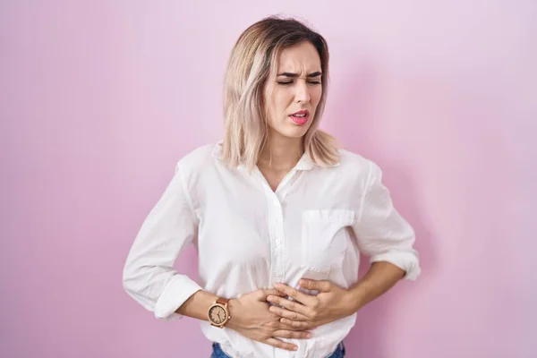 年轻美丽的女人站在粉红的背景上 双手放在肚子上 因为消化不良 痛苦不堪 疼痛的概念 — 图库照片