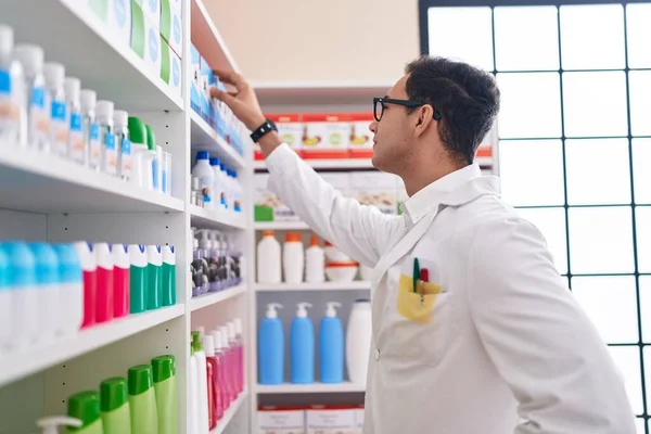 若いヒスパニック系の男性薬剤師が薬局で棚に製品を保持 — ストック写真