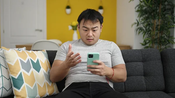 Joven Hombre Chino Usando Teléfono Inteligente Con Expresión Preocupada Casa —  Fotos de Stock