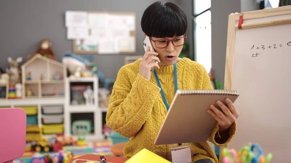 中国の若い女性就学前の先生が幼稚園でスマートフォンの読書ノートブックで話す — ストック写真