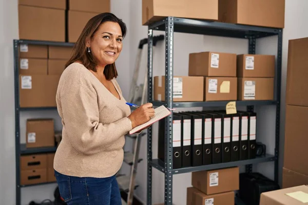 Middle age hispanic woman ecommerce business worker writing on notebook at office