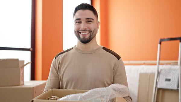 Молодой араб улыбается уверенно держа картонную коробку в новом доме