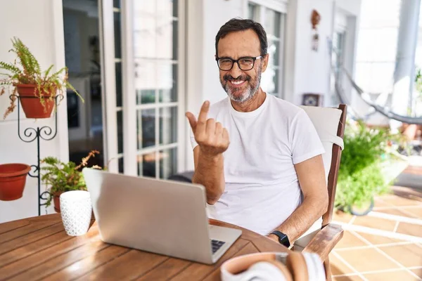 Middle age man using computer laptop at home beckoning come here gesture with hand inviting welcoming happy and smiling