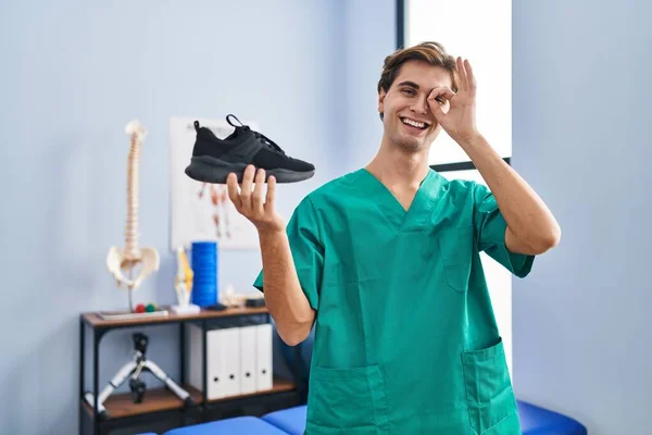 Mladý Muž Pracující Fyzioterapeutické Klinice Drží Boty Úsměvem Šťastný Dělá — Stock fotografie