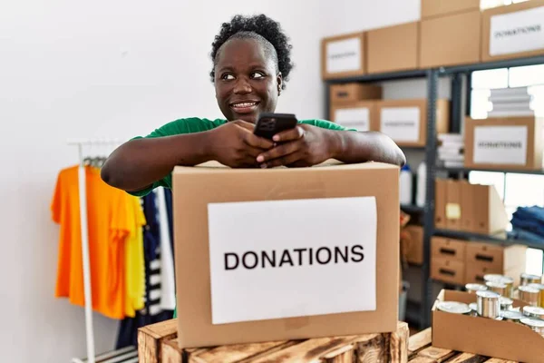 Young african american woman wearing volunteer uniform using smartphone at charity center