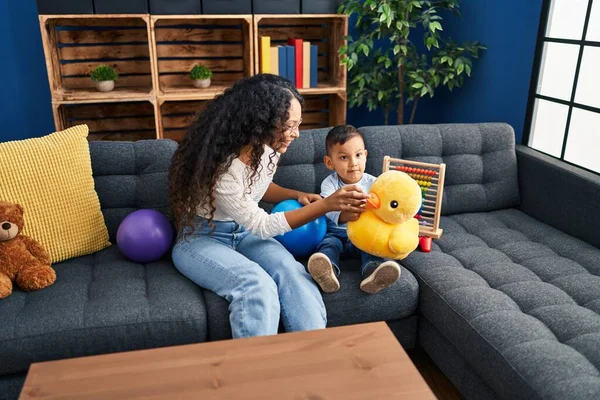 Mother and son playing with toys sitting on sofa at home
