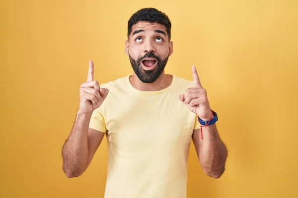 Hispanic Man Beard Standing Yellow Background Amazed Surprised Looking Pointing — Fotografia de Stock