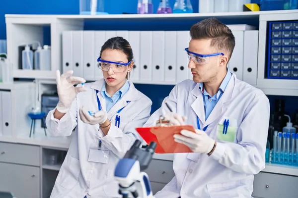 Kadın ve erkek bilim adamları ellerinde haplar tutuyor. Laboratuvarda belgelere yazıyorlar.