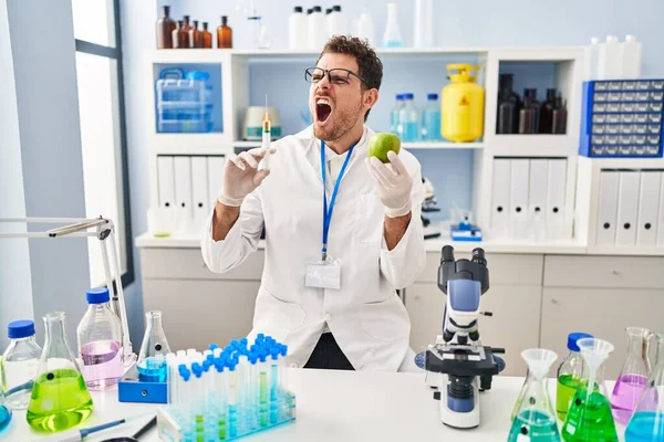 Young Hispanic Man Working Scientist Laboratory Holding Apple Angry Mad — Stockfoto