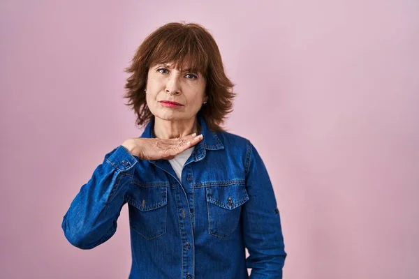 stock image Middle age woman standing over pink background cutting throat with hand as knife, threaten aggression with furious violence 