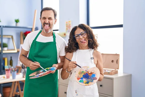 stock image Middle age hispanic couple painting at art studio sticking tongue out happy with funny expression. 