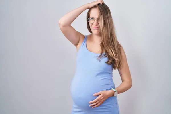 白い背景の上に立つ若い妊婦は混乱し 質問について疑問に思う 疑いもなく頭に手を置いて考える 包括的な概念は — ストック写真