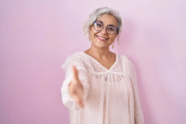 中年妇女灰白的头发站在粉红的背景上 微笑友好地握手致意和欢迎 成功的商业 — 图库照片