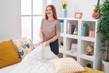Young redhead woman smiling confident make bed at bedroom