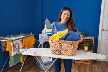 Genç esmer kadın evde ütü yapıyor, gülüyor ve kahkahalarla gülüyor.. 