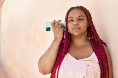 Afro-Amerikalı kadın gülümsüyor. Caddedeki akıllı telefondan kendine güvenen sesli mesaj dinliyor.