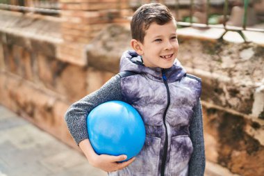 Sarışın çocuk gülümsüyor kendine güvenen topu sokakta tutuyor